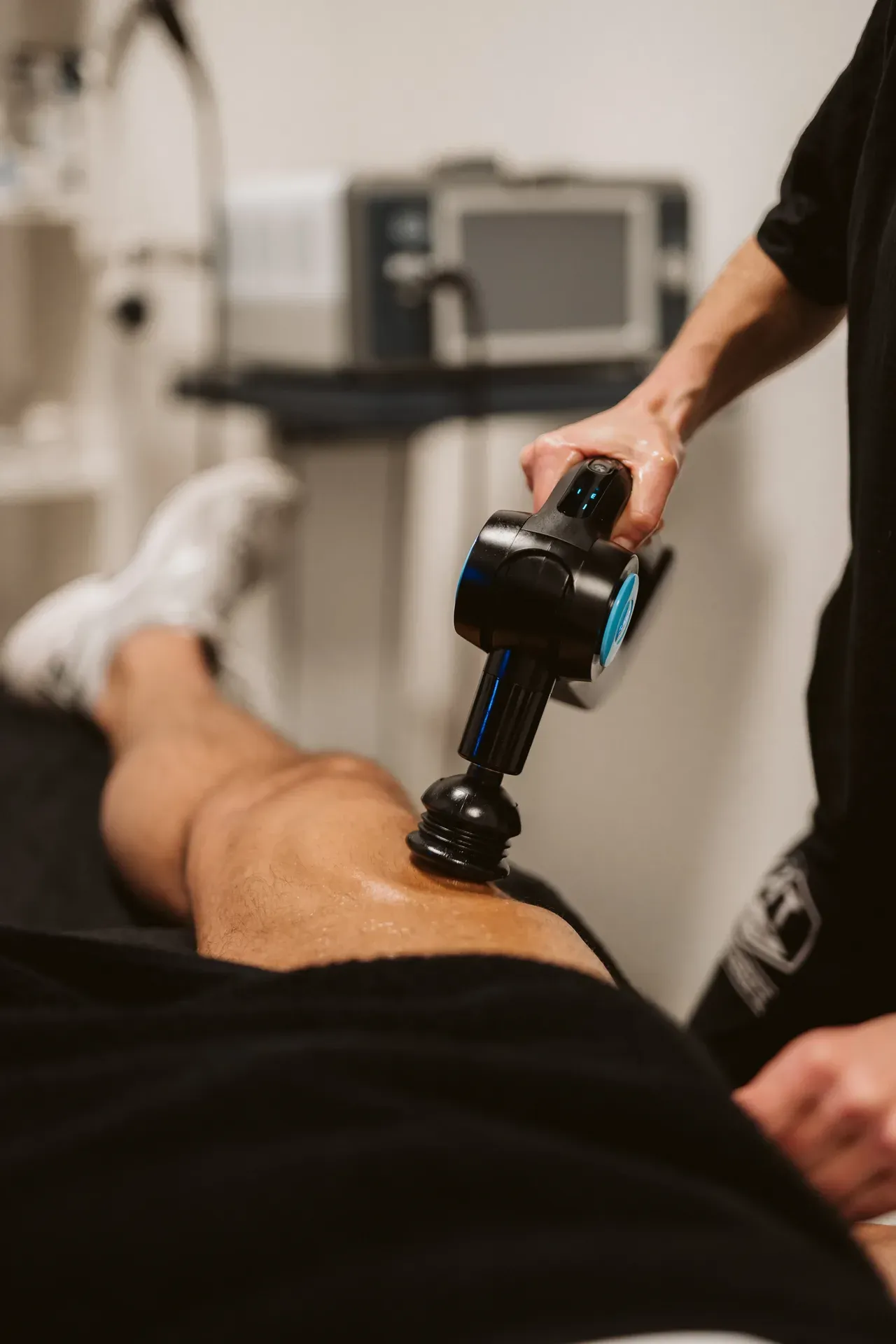 Massagegun behandeling van het bovenbeen op de behandelbank