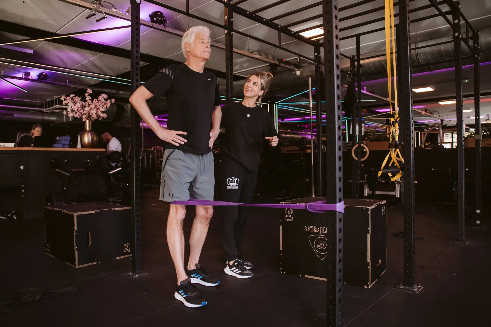 Fysiotherapeut en cliënt bij een balansoefening met weerstandsband in de gym