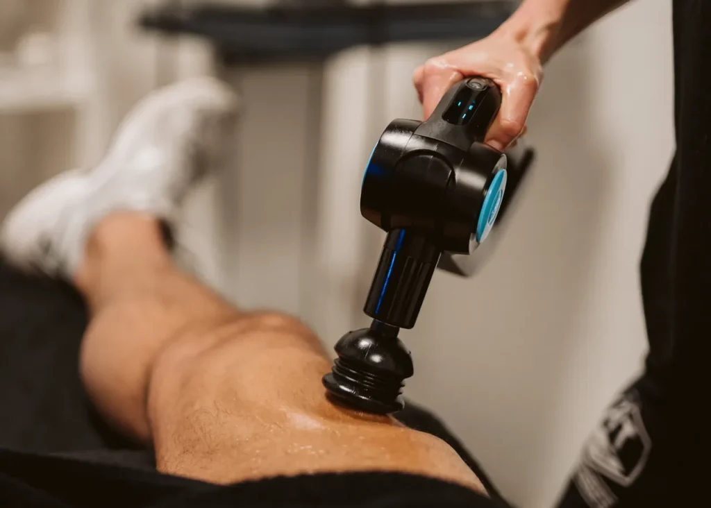 Massagegun behandeling van het bovenbeen op de behandelbank