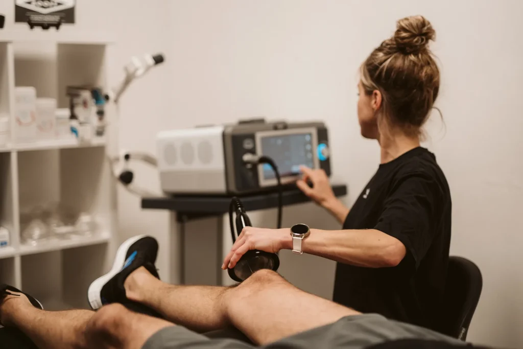 Shockwave behandeling van het been, de fysiotherapeut bedient het apparaat